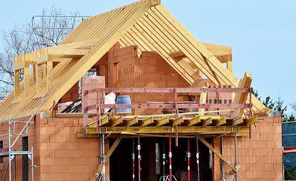 Houten dakconstructie in aanbouw met spanten en balken boven een metselwerk huisframe.